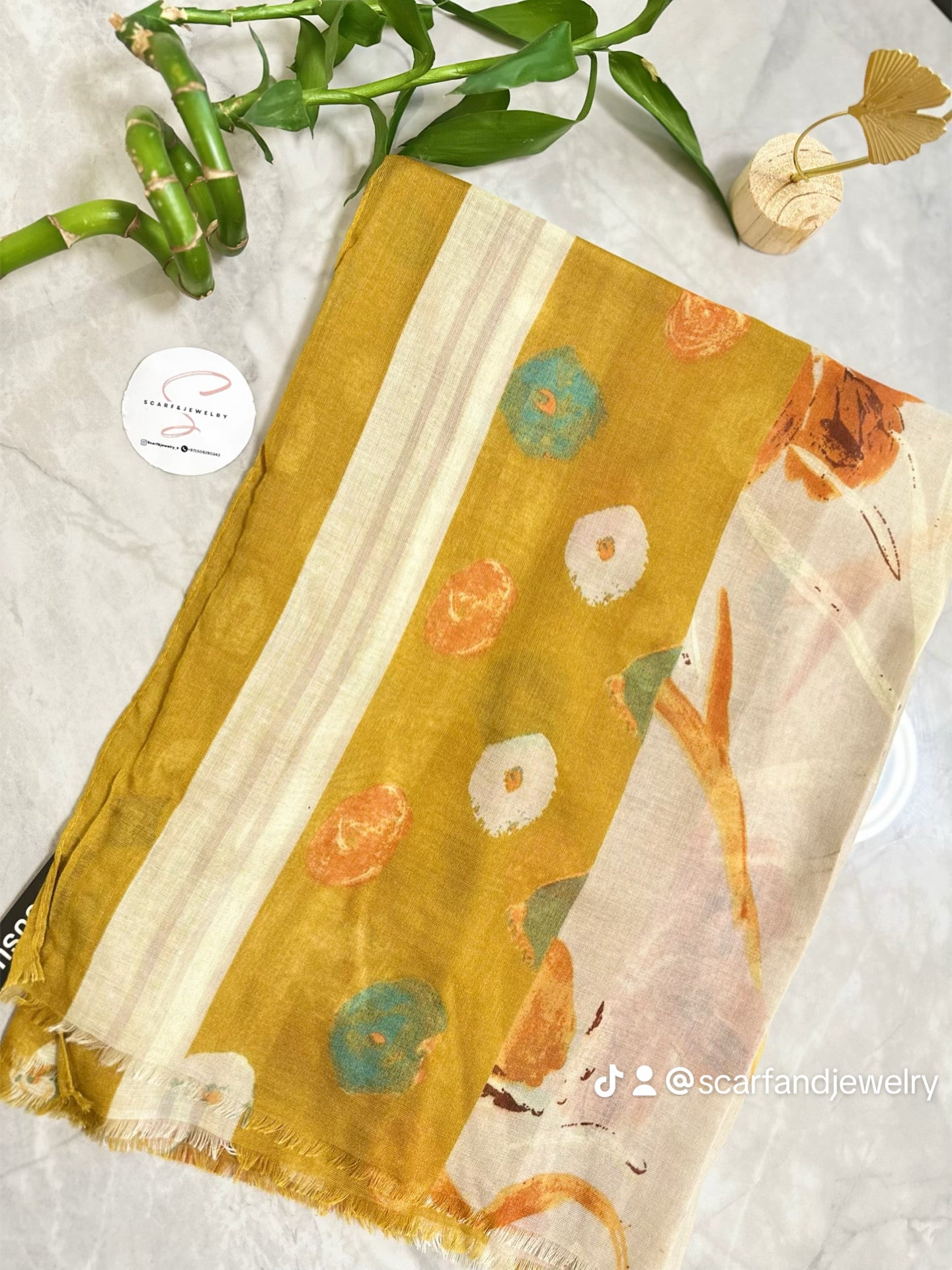Yellow floral scarf on a light background with a plant and jewelry box.